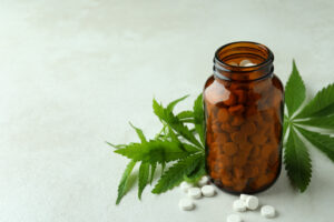 Bottle with pills and cannabis leaves on white textured background